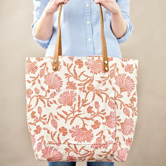 Person holding a large printed tote bag with pocket and leather straps.