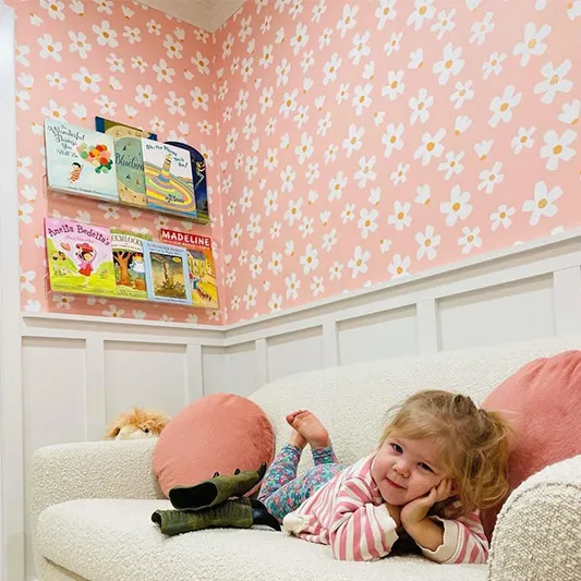 Pink daisy wallpaper above a reading area with little girl on couch.