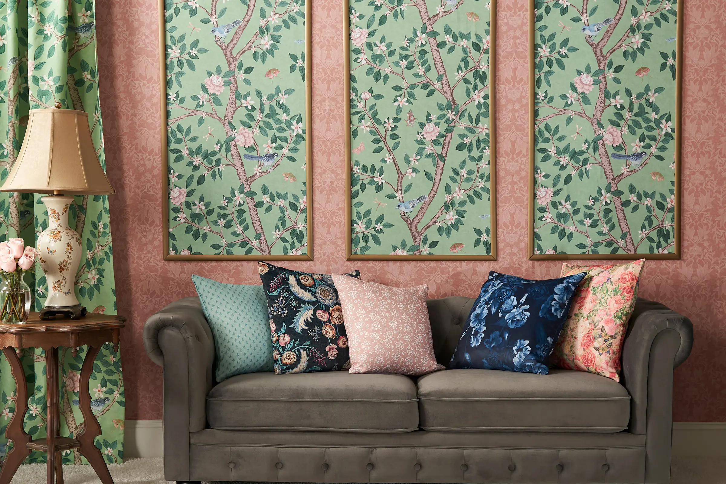 Living area with pink and green floral wallpaper, pillows and curtains.