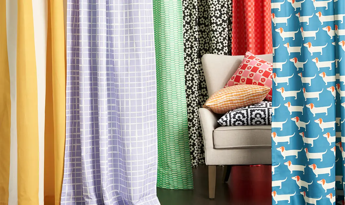 Multiple colorful curtains hanging around a chair with throw pillows