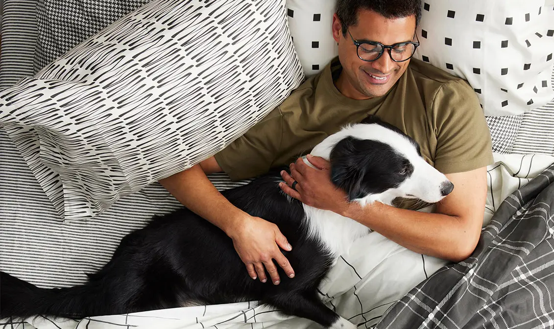 Man snuggling dog in black and white bedding